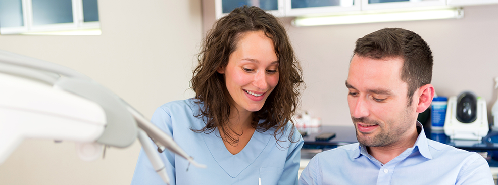 Female dentist standing next to male dental patient