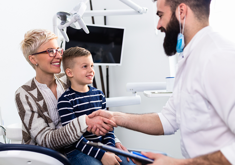 Patient with child on lap shaking hands with dentist