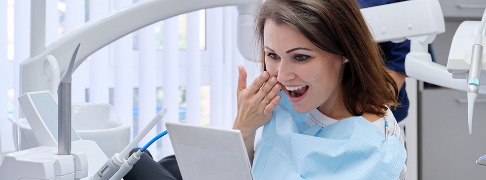 Female patient sitting in dental chair checking smile in mirror