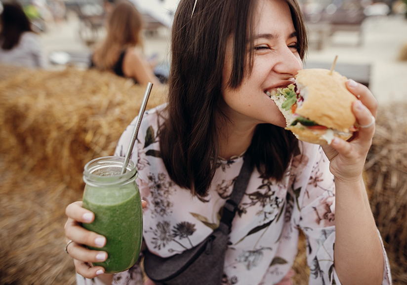 Woman eating burger and holding green shake