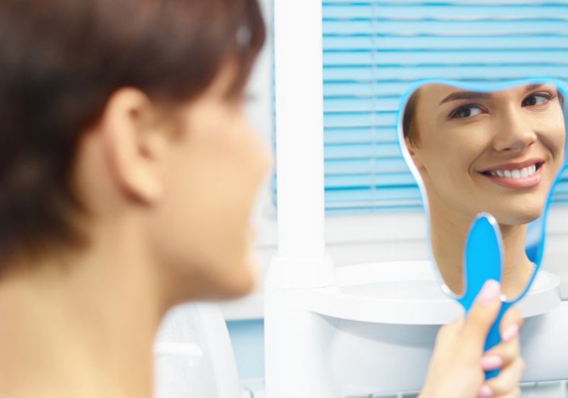 Woman smiling in the mirror after learning cost of cosmetic dentistry in Pantego