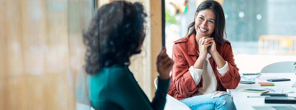 Woman sitting in chair talking to another woman