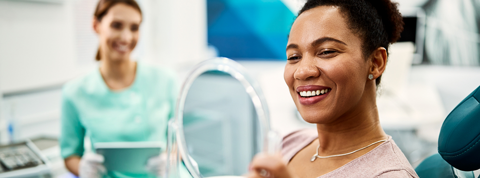 Woman in dental chair checking smile in mirror