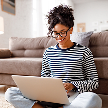 Woman sitting in front of couch typing on laptop