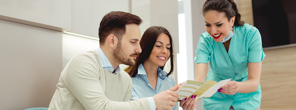 Man and woman looking at brochure held by female dentist