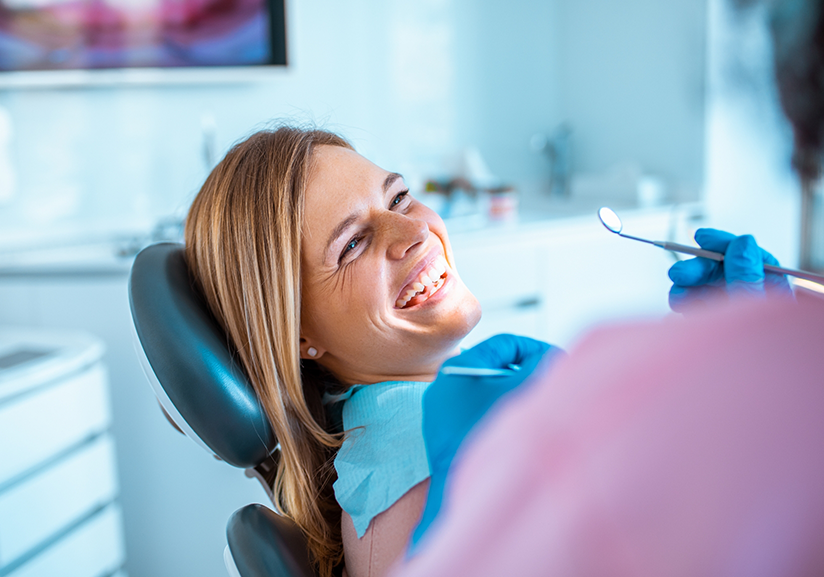 Woman sitting in dental chair smiling up at dentist