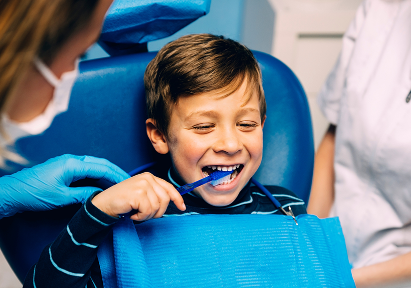 Close-up of little boy in dental chair brushing teeth