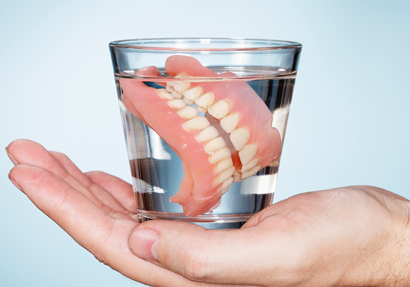 Hand holding glass of water containing dentures