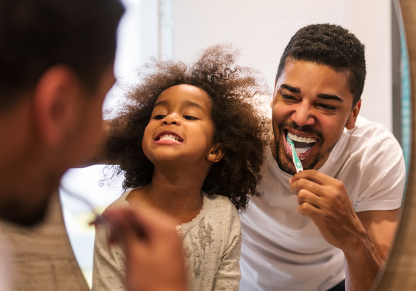 Father and daughter brushing teeth in mirror