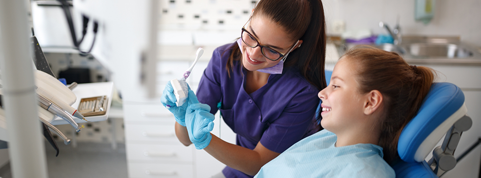 Dentist showing child patient toothbrush and model of teeth