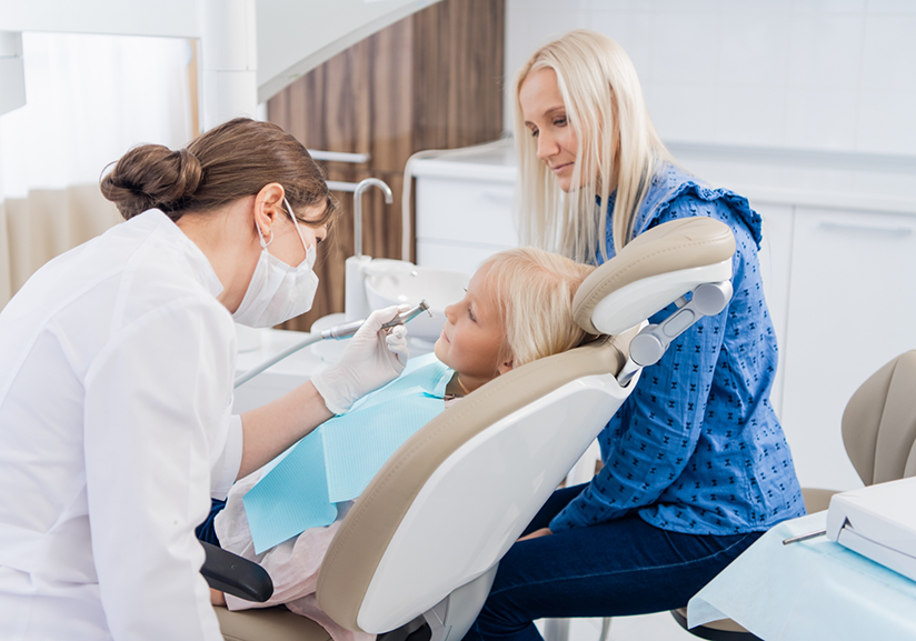 Child in dental chair with mother and dentist nearby