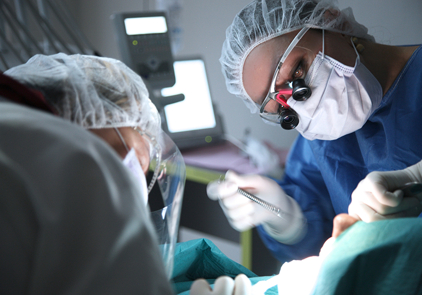 Dentists with masks and surgical hairnets treating patient