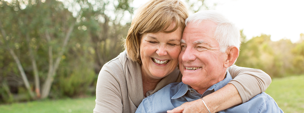 Senior woman hugging senior man from behind