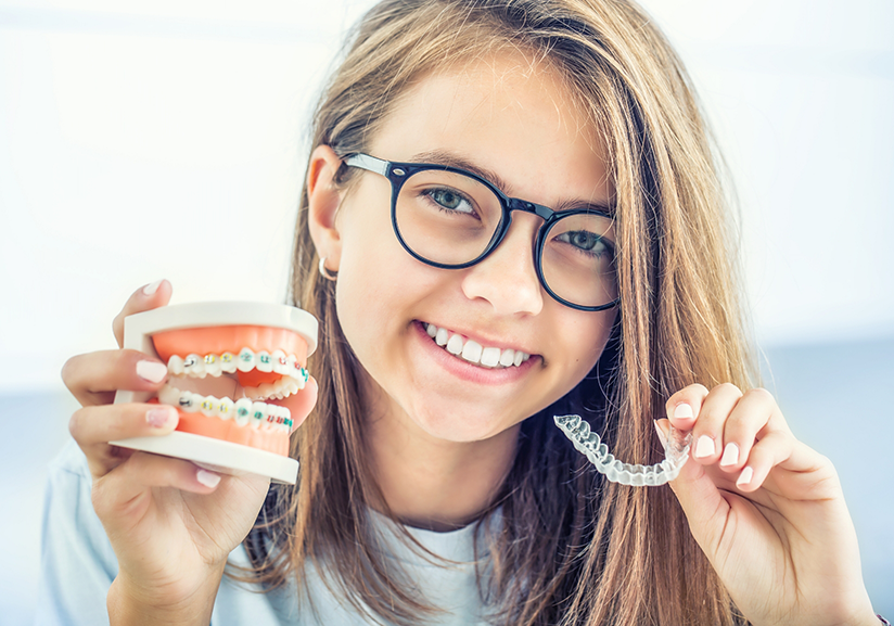 Woman with glasses holding Invisalign aligner and model of teeth with braces