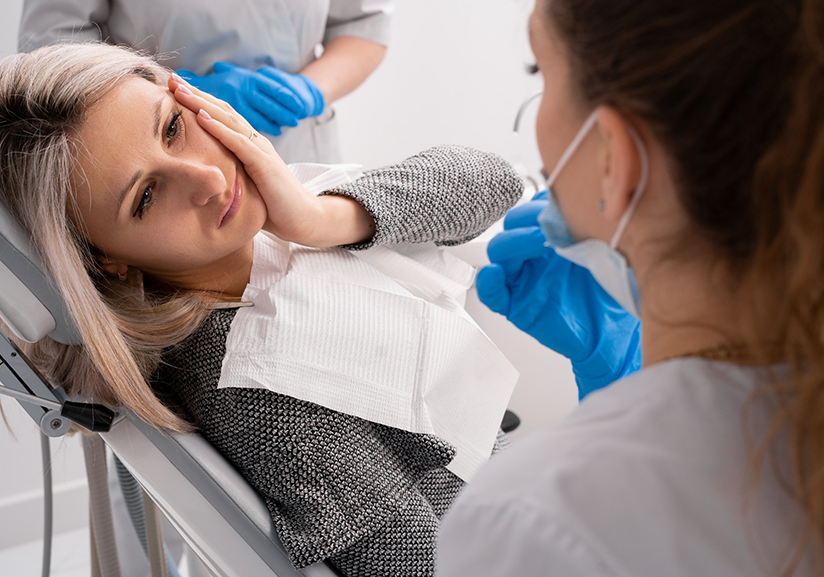 Woman in dental chair rubbing her jaw in pain