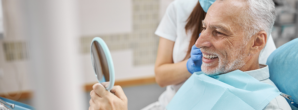 Man in dental chair checking smile in mirror