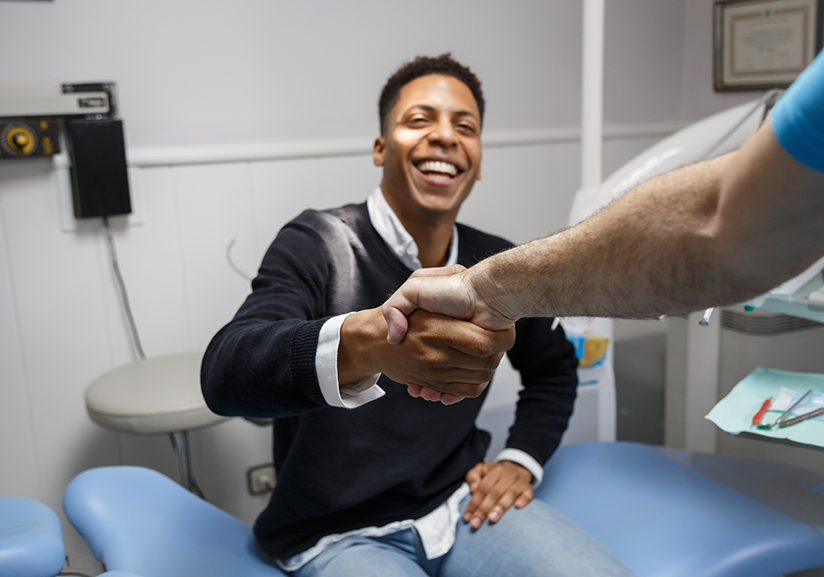 Young man in dental chair shaking dentist's hand