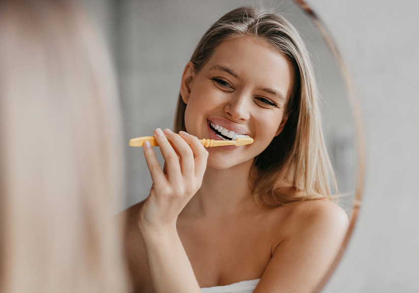 Woman brushing her teeth in bathroom mirror