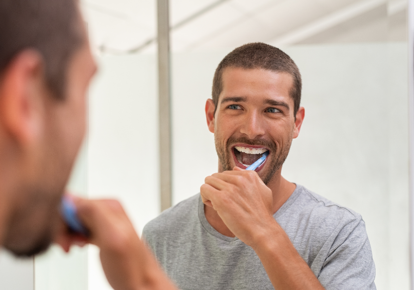 Man brushing his teeth in bathroom mirror