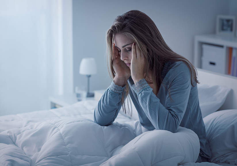 Woman sitting up in bed rubbing temple