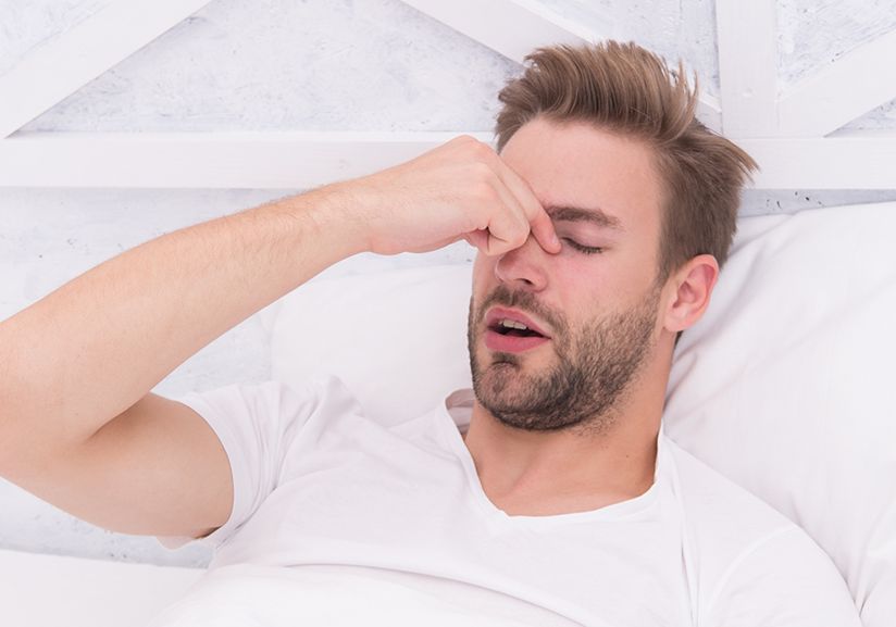 Man lying in bed rubbing bridge of nose