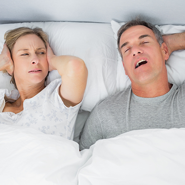 Man snoring in bed with woman covering ears