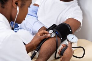 Medical professional in white coat measuring blood pressure of a patient in a white shirt